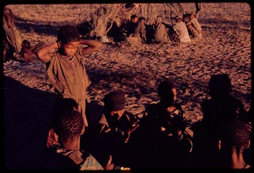 Group of women sitting in a circle and clapping, with a boy, probably Gaoxa (son of N≠isa n!a), standing nearby