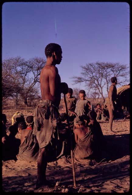 /Gaishay and /Xoxa standing for a curing dance, with a group of women sitting in a circle in the middle