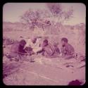 Expedition: Gau fixing Laurence Marshall's shoe by making a hole with an awl and sticking thread through the hole, with "Gao Medicine" and ≠Toma sitting with them