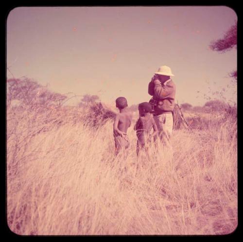 Expedition: Two boys standing with Laurence Marshall who is taking a photograph with a Leica camera