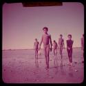 Scenery: /Qui (son of "/Gao Music") walking through shallow water in a pan, with a group of boys behind him