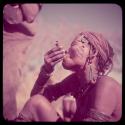 Smoking: Woman wearing blue beads in her hair, smoking a pipe made from a cartridge