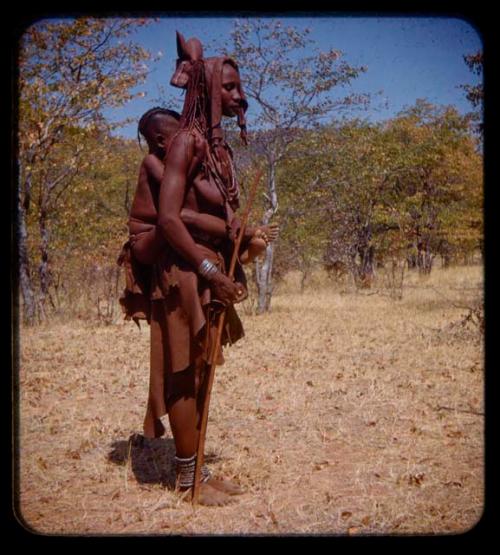 Woman carrying a child on her back and holding a stick in her hand