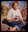 Elizabeth Marshall Thomas sitting and holding a plasticene model of animal made by a Ju/'hoan boy