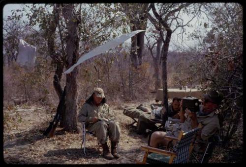 O.P.M. Prozesky, C.J. Mathias, and Kurt Ahrens sitting at expedition camp in the mangetti forest