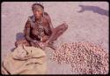 Woman sitting by pile of mangetti nuts, close-up