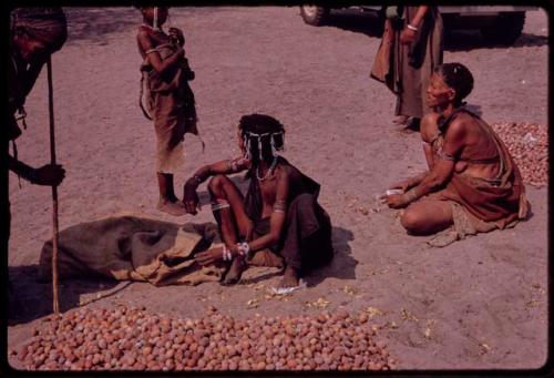 Groups of people sitting by piles of mangetti nuts, "Gao Medicine's" mother to the right