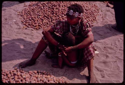 Xama sitting beside her pile of mangetti nuts, baby sitting in front of her