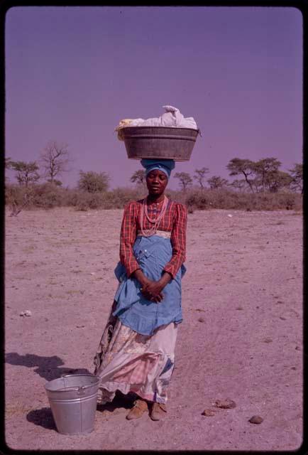 Woman standing with a metal laundry tub on her head