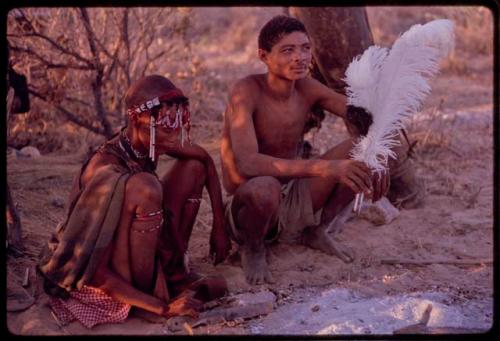 Man and woman sitting, man holding two ostrich feathers