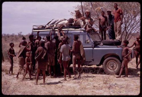 Group of people gathered around an expedition Land Rover, O.P.M. Prozesky and Wulf Haacke sitting with a dead ostrich on top of the Land Rover