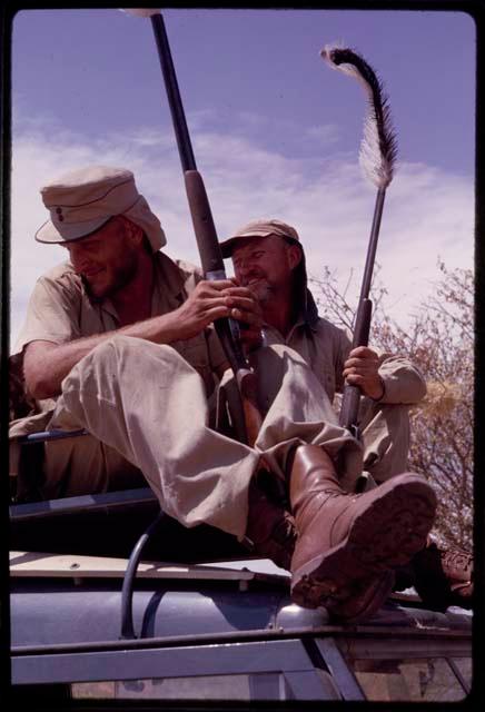 O.P.M. Prozesky and Wulf Haacke sitting with ostrich on top of the Land Rover, close-up