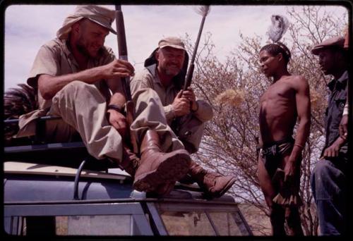 O.P.M. Prozesky and Wulf Haacke sitting with ostrich on top of the Land Rover, two men standing on the truck hood next to them