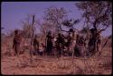 O.P.M. Prozesky, Wulf Haacke, and other expedition members standing with a group of people watching the cutting up of an ostrich, seen from behind in the distance