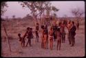 Adults gathering for a curing dance, women clapping and children dancing