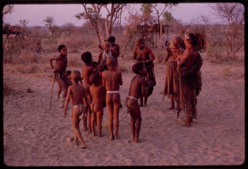 Adults gathering for a curing dance, women clapping and children dancing