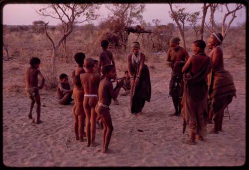 Adults gathering for a curing dance, women clapping and children dancing