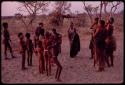 Adults gathering for a curing dance, women clapping and children dancing