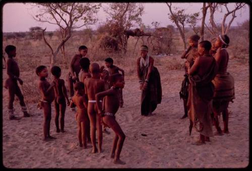 Adults gathering for a curing dance, women clapping and children dancing