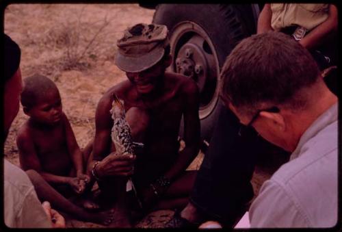 Group of people sitting with O.P.M. Prozesky, Nicholas England, Dabe, and Lorna Marshall and identifying birds; man holding a bird, close-up