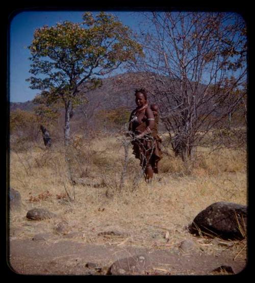 Woman with a baby on her back standing in grass