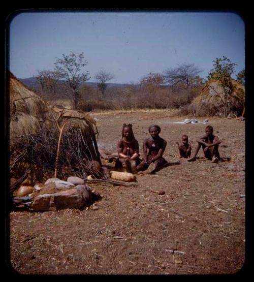 Cavale, Boalemuhung's wife, a boy, and a child sitting outside a hut