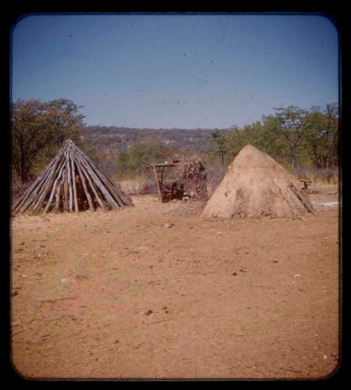 People sitting in the shade in Mukolovandi's kraal; hut and storage hut, seen in the distance