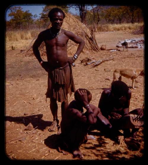 Mukolovandi standing; Mukolovandi's cousin and Kanakele sitting while Kanakele plays a chihumba