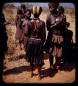 Group of people standing by a road; woman standing showing back of a headdress