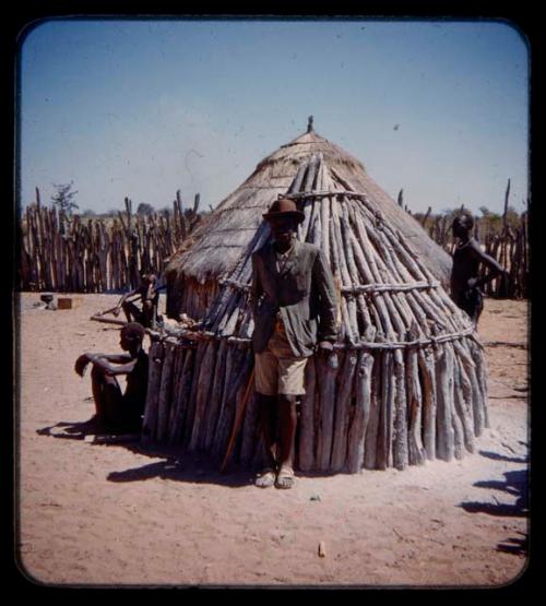 Man standing in front of a hut, people in the background