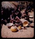 Group of women sitting in front of a hut with bowls in front of them