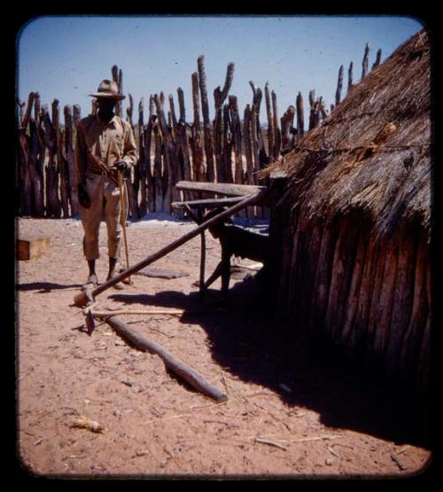 Girl crawling out of a hut, Headman standing near the door