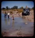 Expedition members standing in a river, expedition truck on road