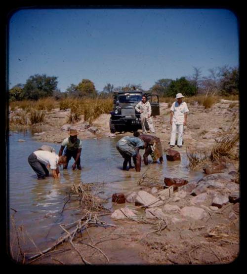 Expedition members pulling up rocks from the riverbed, expedition truck in the background