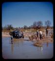 Expedition truck in a river, expedition members standing around