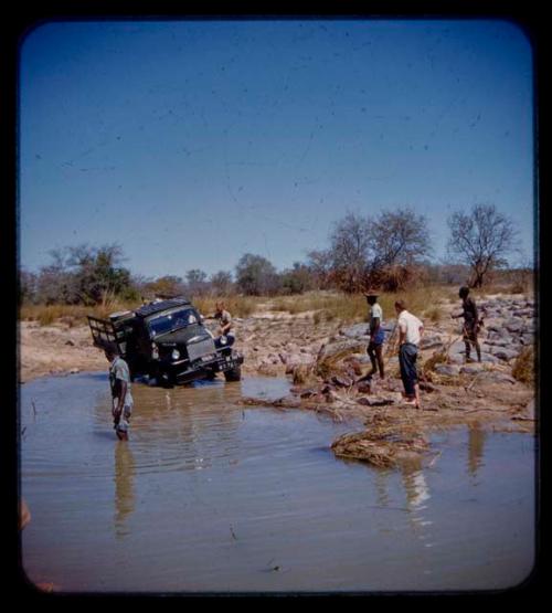 Expedition truck in a river, expedition members standing around