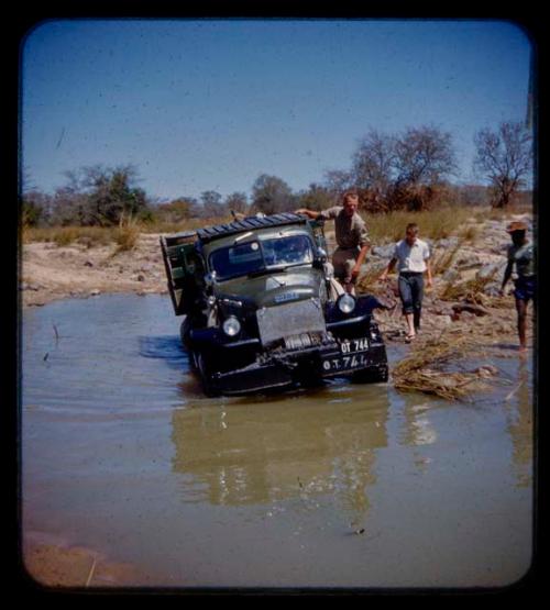 Expedition truck in a river, expedition members standing around