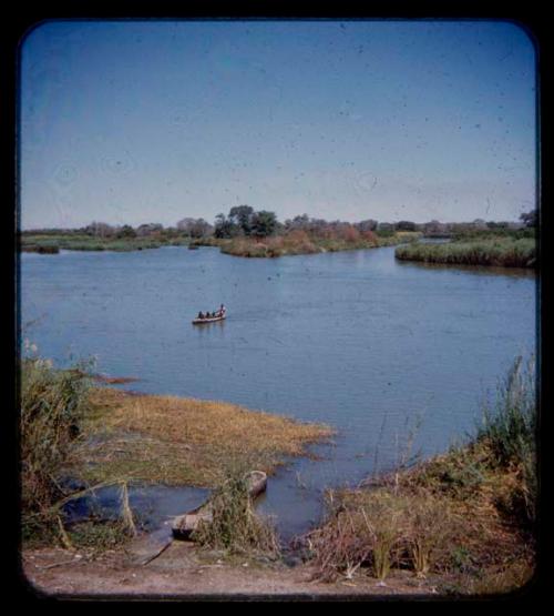 Expedition members in a canoe crossing a river, seen from a distance