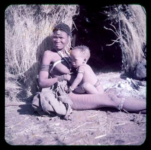 Children, Mother and children: Woman with scarification on her leg, wearing an under-knee bracelet on her leg, sitting by a skerm holding a baby