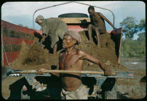 /Ti!kay and two other men shoveling fertilizer from the back of the expedition truck