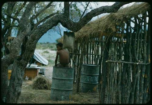 Child sitting on a metal drum next to a cookhouse