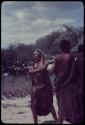 Three women standing, with a kraal fence and trees in the background