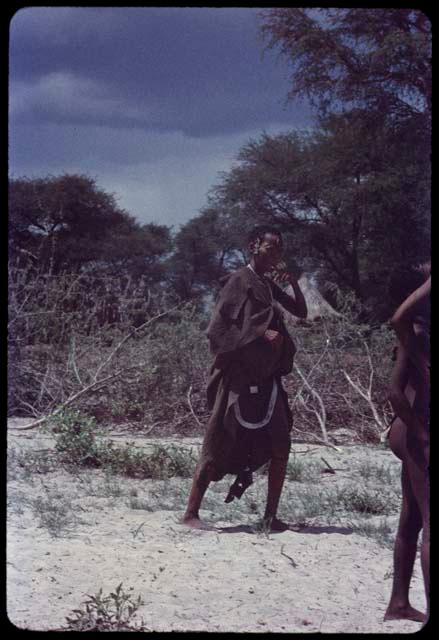 Woman standing in front of a kraal, with a hut in the background