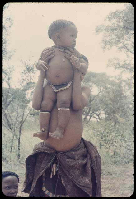 Girl standing, holding up a baby in front of her