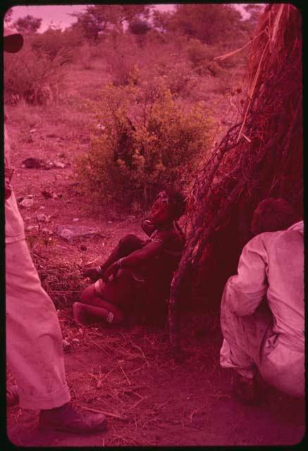 Di!ai sitting next to a skerm, nursing a child, with two expedition members next to her