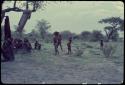 Group of people sitting next to a tree with a blanket hanging in it, children walking near them