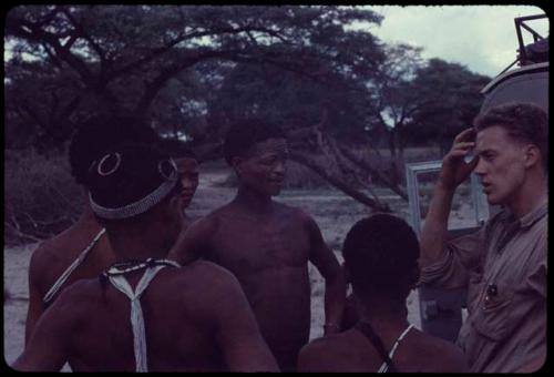 Group of people standing with /Ti!kay and John Marshall next to the expedition Land Rover