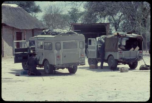 Expedition trucks parked next to a brick building with a thatched roof