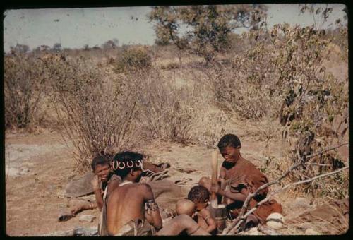 Children, Mothers: //Khuga (wife of !Naishi, headman of Band 5) pounding something in a mortar, sitting with Khwo//o (mother of "/Gao Music" and /Goishay), !U, !Ungka Norna and another child (copy of slide 7A-97)