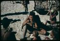 Woman sitting with a group of people, with a child drinking juice from a tsama melon behind her (copy of slide 11E-1)